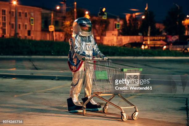 spaceman in the city at night on parking lot with shopping cart - future retail stock pictures, royalty-free photos & images