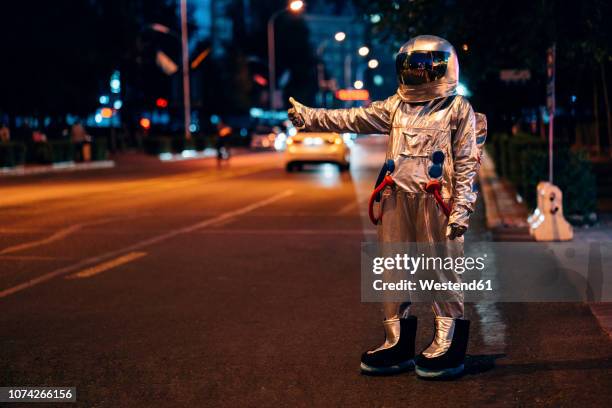 spaceman standing on a street in the city at night hitchhiking - eccentrico foto e immagini stock