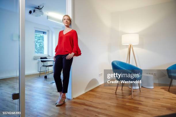 portrait of young woman leaning against doorframe in office - lean imagens e fotografias de stock