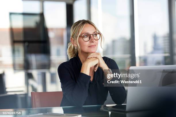 businesswoman sitting at desk, thinking - une seule femme d'âge mûr photos et images de collection