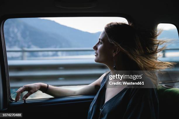 young woman sitting on backseat in a car looking out of window - fahrgastsitz stock-fotos und bilder