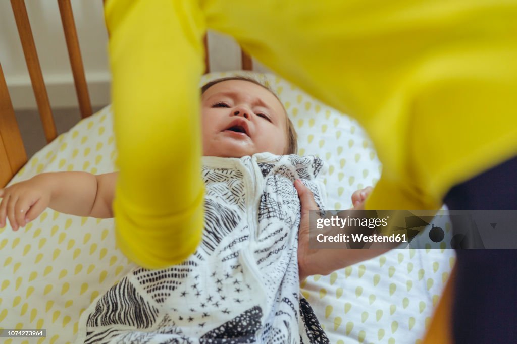 Mother picking up her baby girl from bed