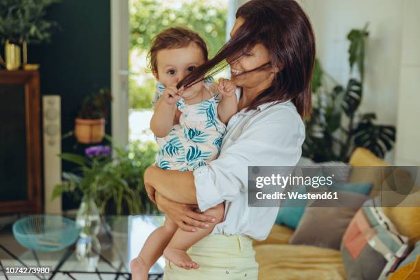 baby girl pulling mother?s hair in living room - pulling fotografías e imágenes de stock