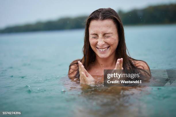 portrait of freckled young woman  bathing in lake on rainy day - rain smiling stock-fotos und bilder