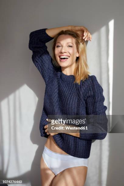 portrait of laughing blond woman wearing knit pullover and panties leaning against wall - mid adult women stock pictures, royalty-free photos & images