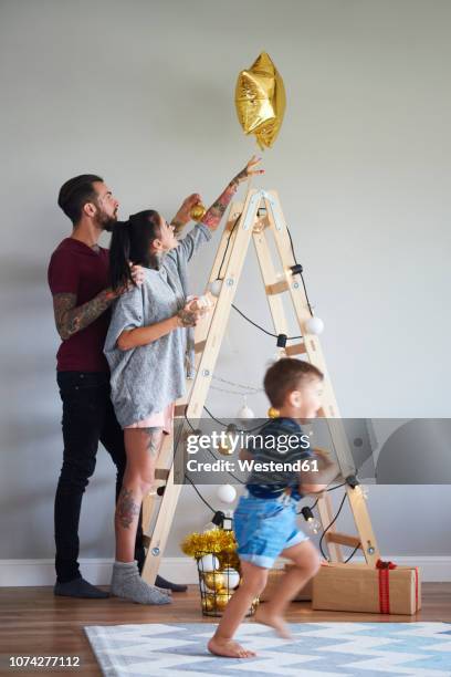 modern family decorating the home at christmas time using ladder as christmas tree - renegades v stars stockfoto's en -beelden