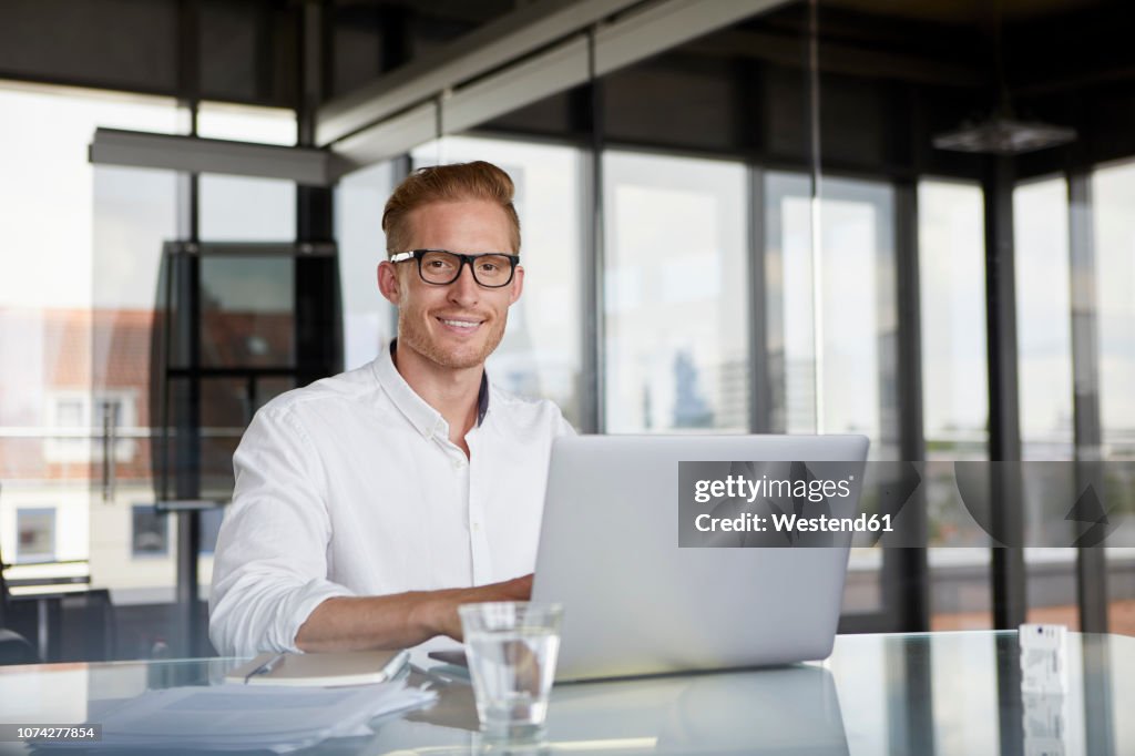Portrait of smiling businessman using laptop on desk in office