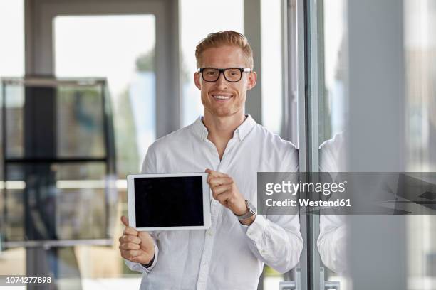portrait of smiling businessman showing tablet at the window in office - tonen stockfoto's en -beelden