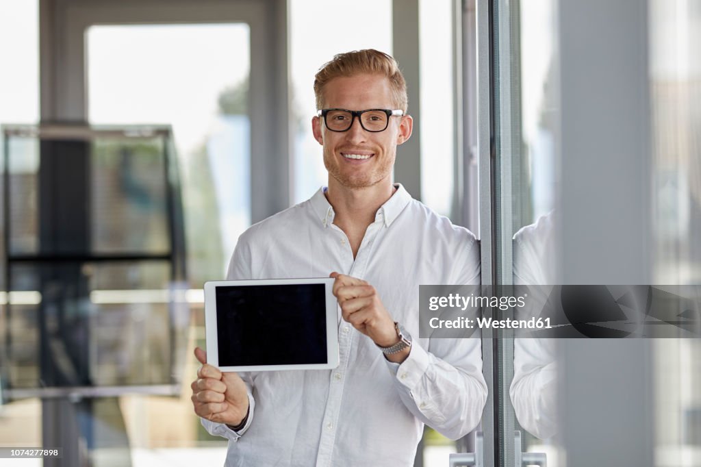 Portrait of smiling businessman showing tablet at the window in office