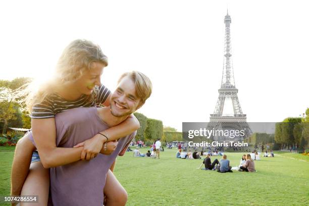 young couple doing piggyback in front of eiffel tower - park couple piggyback stock pictures, royalty-free photos & images