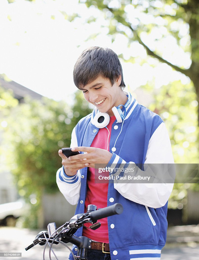 Smiling teenage boy text messaging on cell phone