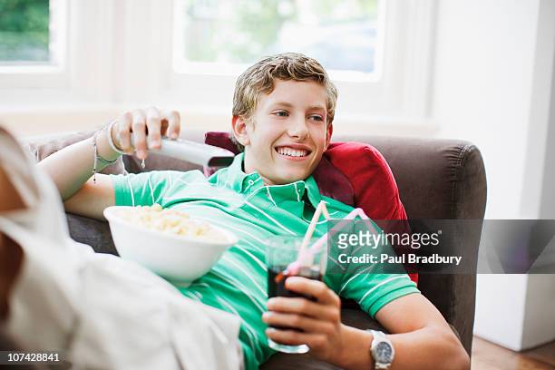 teenage boy with snacks holding remote control - boy at television stockfoto's en -beelden