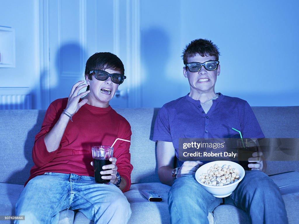 Teenage boys with snacks watching television with 3-D glasses