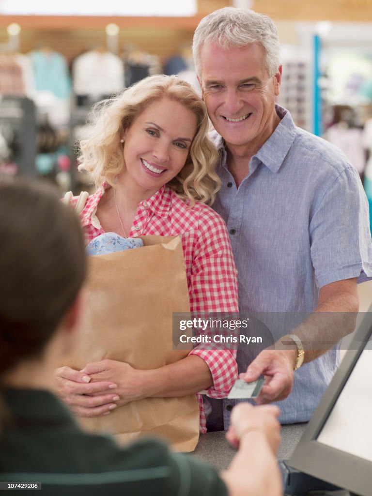 Casal sorridente com saco de compras entregar o cartão de crédito na caixa