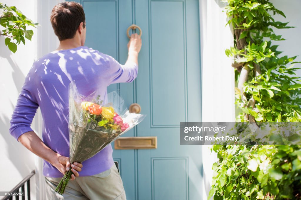 Man holding bouquet of flowers and knocking on door