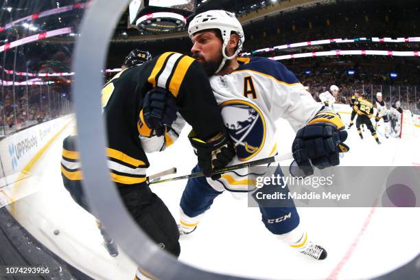 Zach Bogosian of the Buffalo Sabres checks Danton Heinen of the Boston Bruins into he boards in the first period of the game between the Boston...