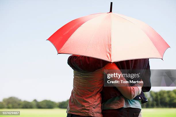 couple hugging underneath red umbrella - red parasol stock pictures, royalty-free photos & images