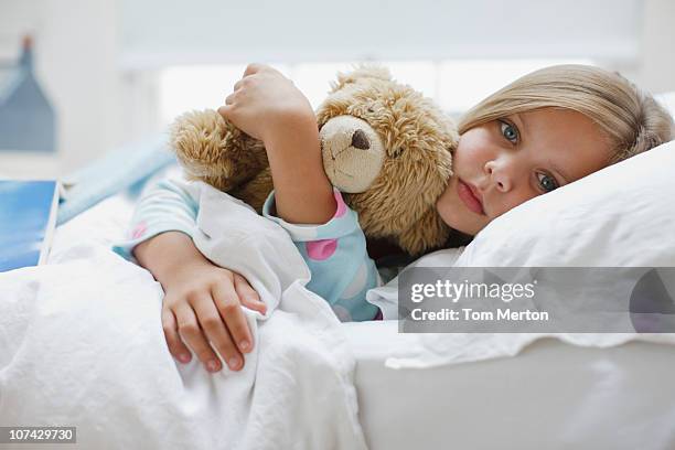 sick girl laying in bed with teddy bear - sick child stockfoto's en -beelden