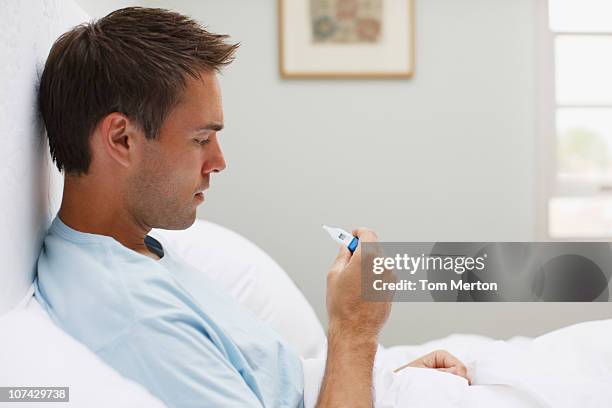 sick man taking temperature with digital thermometer - fever stock pictures, royalty-free photos & images
