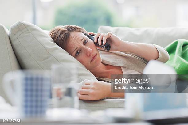 mujer enferma sentar en el sofá hablando por teléfono - illness fotografías e imágenes de stock