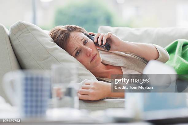 sick woman laying on sofa talking on telephone - illness stock pictures, royalty-free photos & images