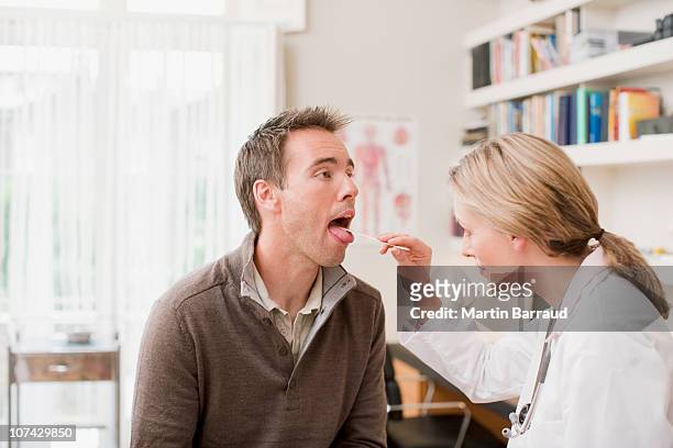 doctor examining patients throat in doctors office - sticking out tongue stock pictures, royalty-free photos & images