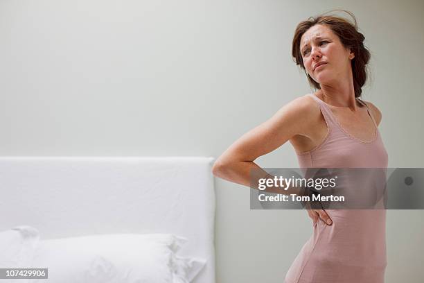 woman rubbing aching back in bedroom - back pain bed stock pictures, royalty-free photos & images