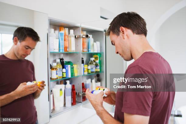 man looking at bottles from medicine cabinet - pijnstiller stockfoto's en -beelden