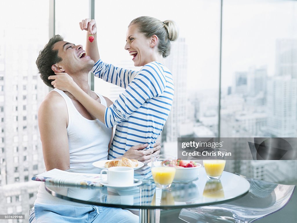 Playful woman feeding strawberry to husband at breakfast