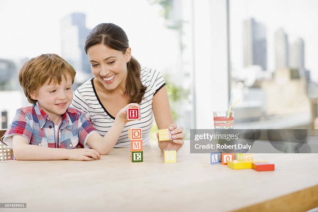 Mother watching son stacking alphabet blocks and spelling home