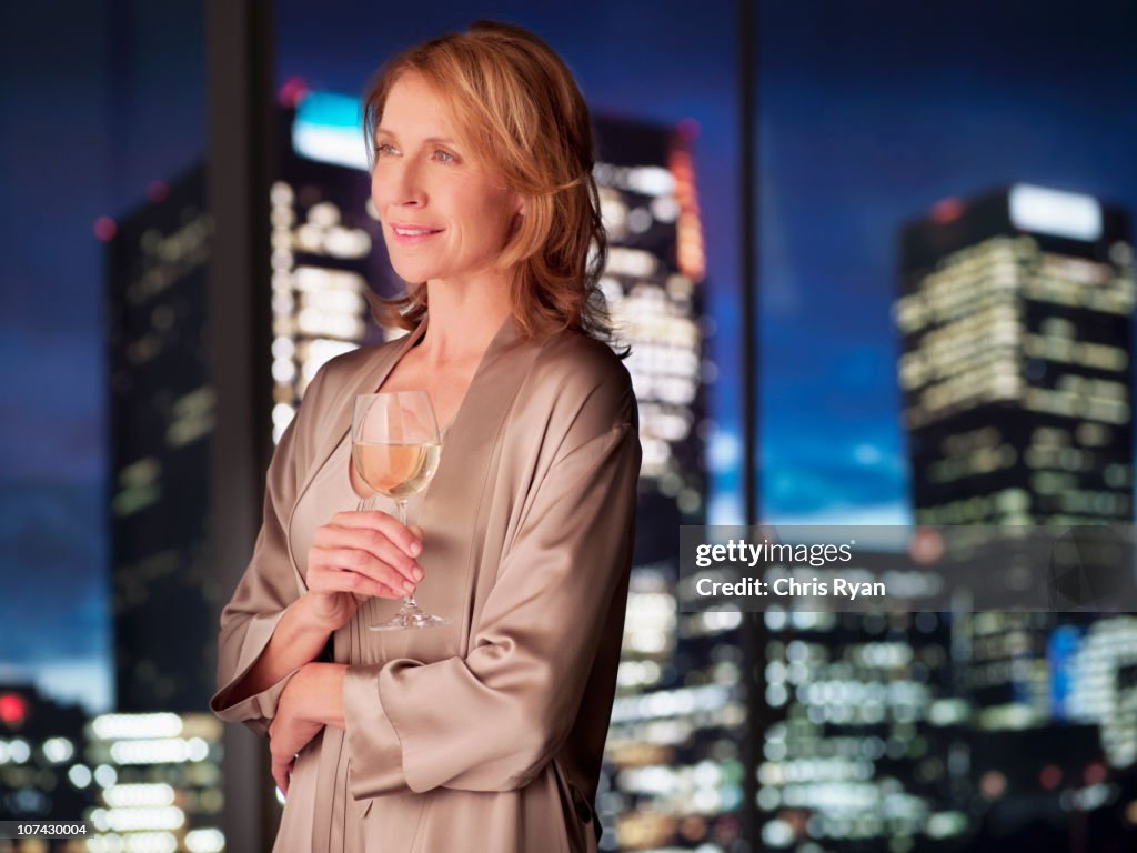 Woman in nightgown drinking white wine at night