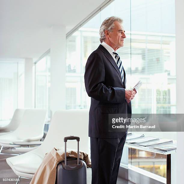hombre de negocios de pie con pasaporte y el equipaje en el aeropuerto - three quarter length fotografías e imágenes de stock