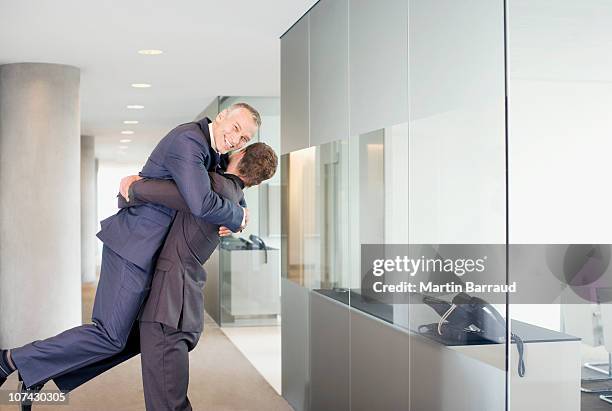 excited businessman lifting co-worker in office corridor - office cheering stock pictures, royalty-free photos & images