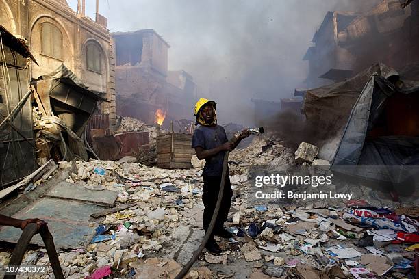 Haitian firefighter stands in the rubble outside the flaming and smoke-filled industrial section of downtown Port au Prince, Haiti. On January 12,...