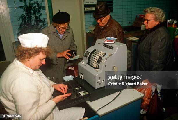 As a staff member counts coins, 1990s women shoppers gather around the till to pay cash in a Budapest shop, on 13th June 1990, in Budapest, Hungary.