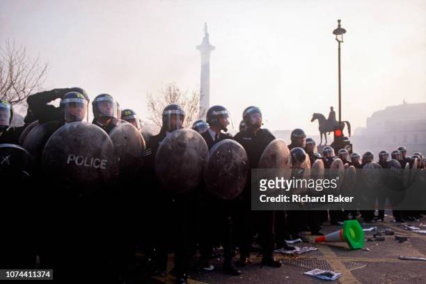 Riot police officers stand firm in Trafalgar Square at the height of the Poll Tax Riot on 31st March 1990, in Westminster, London, England. Angry...