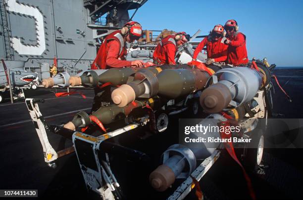 Red-shirted US Navy ordnance crewmen prepare to fit smart bombs and missiles to an F/A-18 fighter jet on the deck of US Navy aircraft carrier USS...