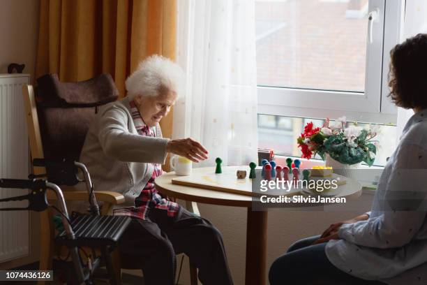 Senior woman playing Ludo game with caregiver