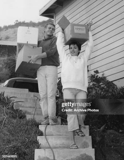 American actor Steve McQueen and his first wife, actress Neile Adams, carry cardboard boxes down their front steps, circa 1958.