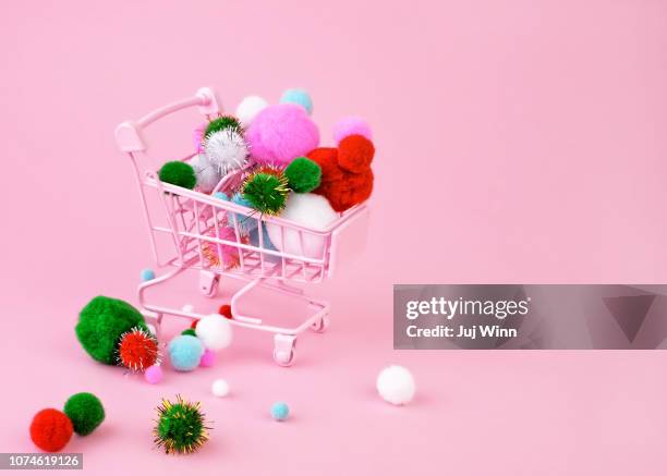 miniature pink shopping cart overflowing with festive pompoms on a pink background. - pom pom stock-fotos und bilder