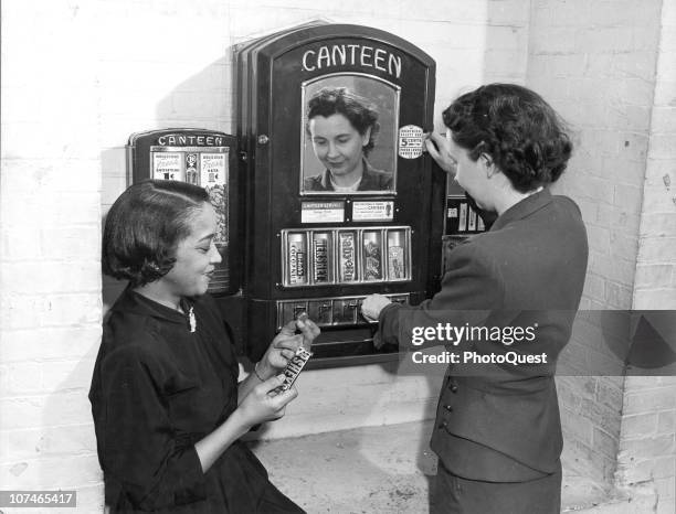 Two office workers are shown using a vending machine, Washington, DC, 1950. They are conveniently located in factories and office buildings, and sell...