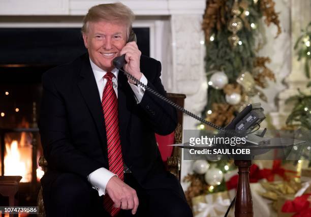 President Donald Trump speaks on the telephone as he answers calls from people calling into the NORAD Santa tracker phone line in the State Dining...