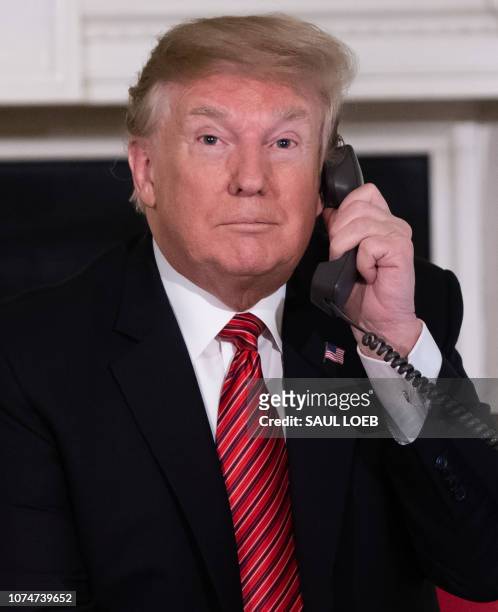 President Donald Trump speaks on the telephone as he answers calls from people calling into the NORAD Santa tracker phone line in the State Dining...