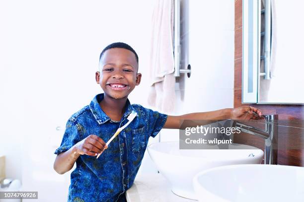 cute african 6-7 years old boy brushing teeth with hand on tap - 6 7 years stock pictures, royalty-free photos & images