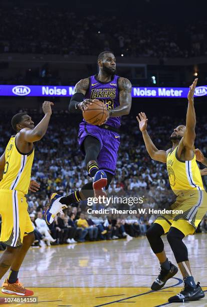 LeBron James of the Los Angeles Lakers leaps in the air to pass the ball between Kevon Looney and Andre Iguodala of the Golden State Warriors during...