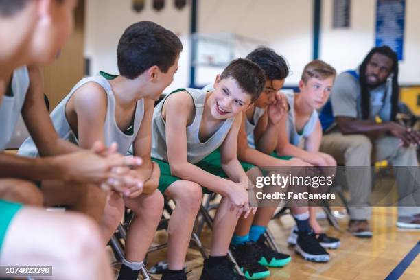 elementary boys basketball team sitting on the sideline bench with their coach - basketball sideline stock pictures, royalty-free photos & images