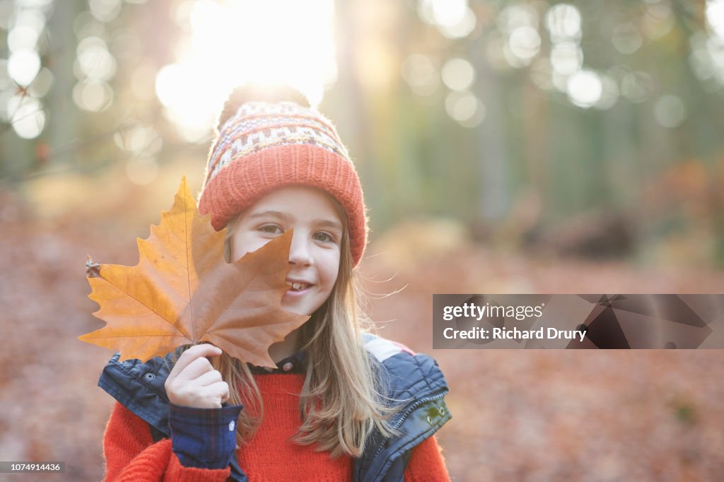 Young girl hiding behind a leaf in Autumnal woodland