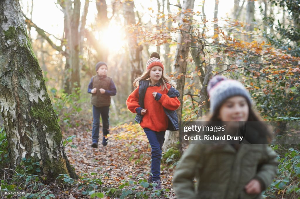 Three children running along a path in Autumnal woodland