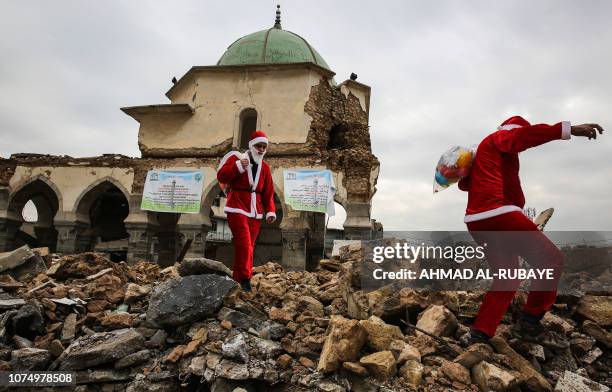 Iraqi youths dressed in Father Christmas suits walk through the ruins of the Great Mosque of Al-Nuri as they distribute gifts in the old city of...