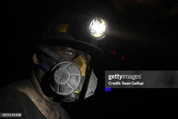 Coal miner's face is covered in coal dust as he wears a mask to prevent coal dust from getting into his lungs approximately 1000 meters below the...